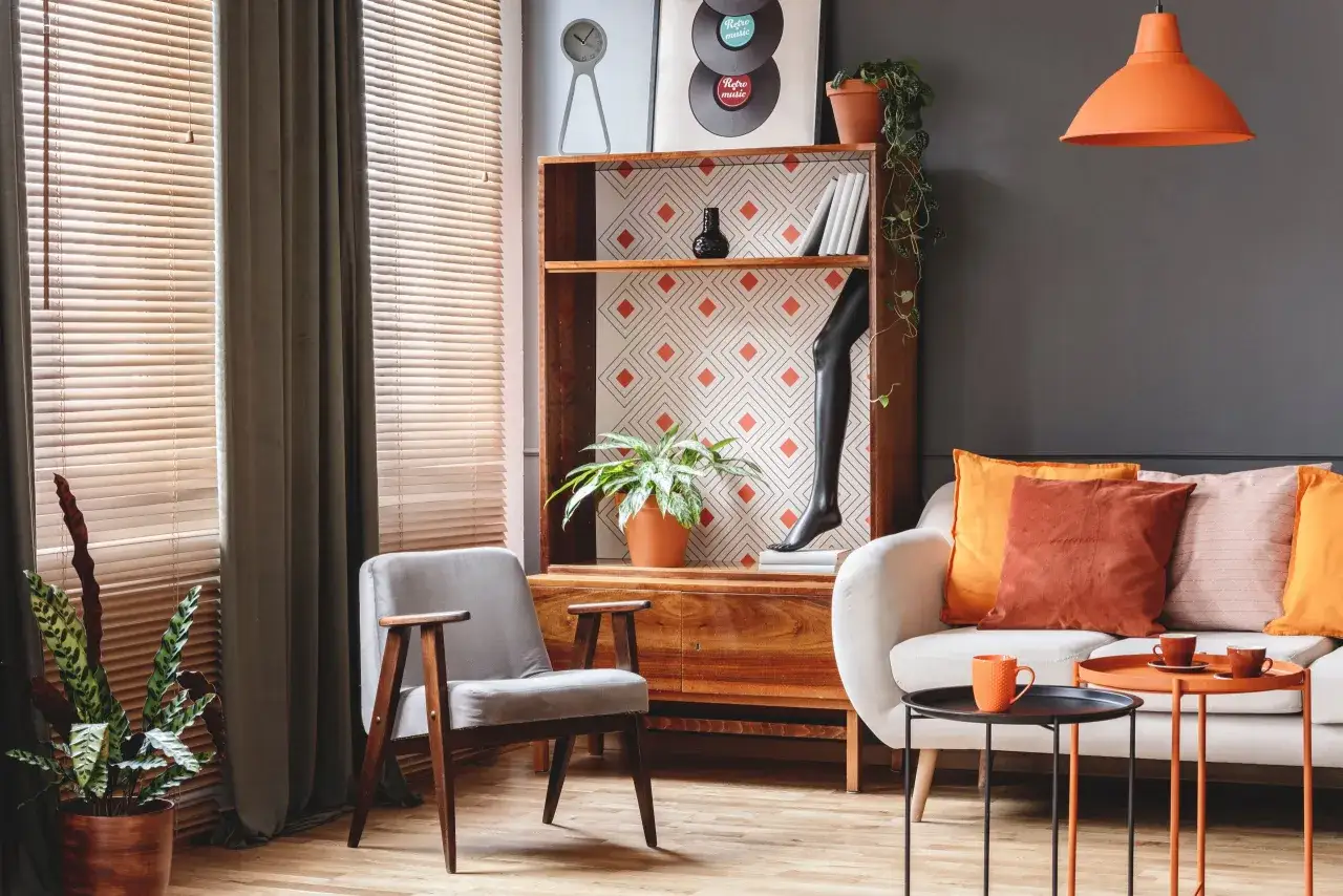 Un salotto con un divano bianco, poltrona grigia e un mobile in legno. L'arredamento vintage casa è completato da cuscini colorati e una lampada arancione.