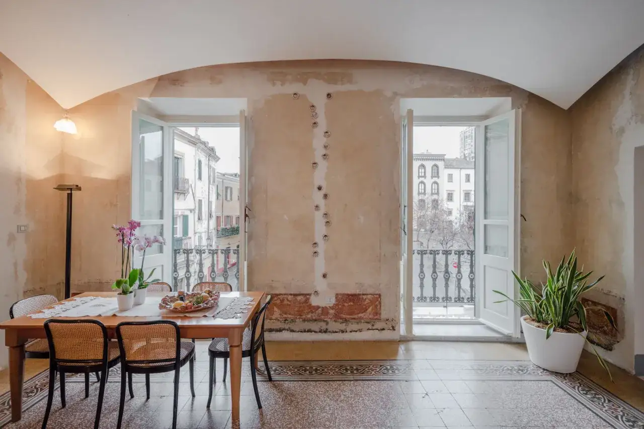 Arredare casa con soffitti a volta: sala da pranzo con vista su palazzi storici, tavolo in legno, sedie in paglia e orchidee.