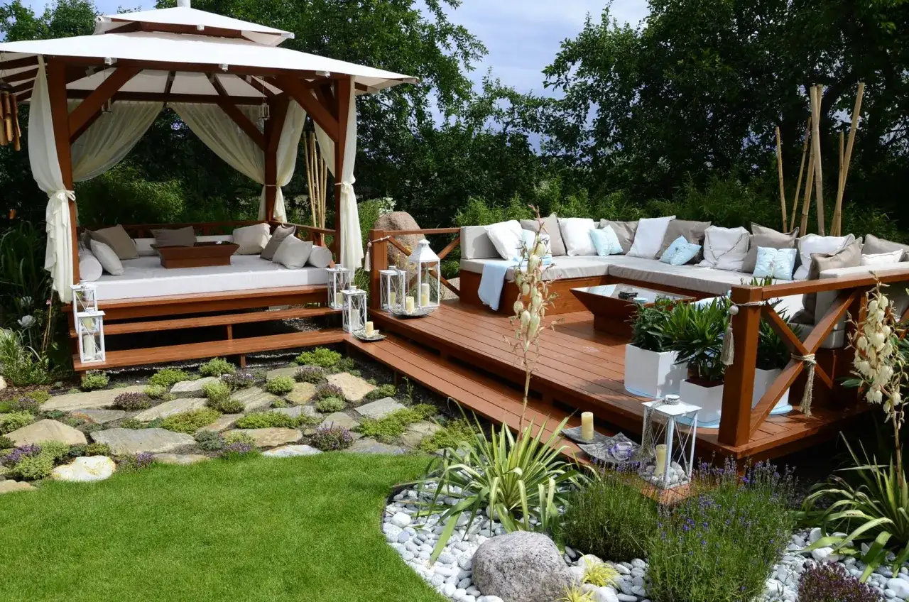Un angolo da sogno per le tue idee zona relax giardino: gazebo con daybed, divano angolare su deck in legno, lanterne e piante.