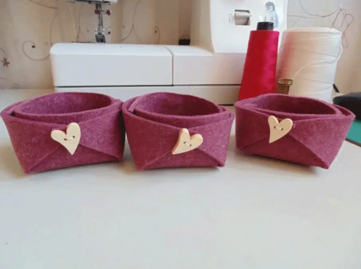 Tre cestini in feltro fai da te, color melanzana, decorati con bottoni a forma di cuore. Perfetti per organizzare piccoli oggetti.