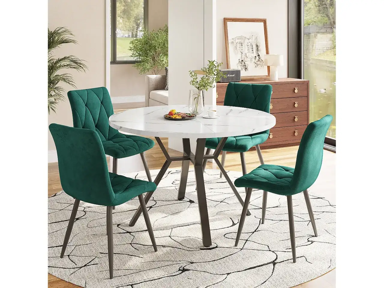 A round marble dining table with four emerald green velvet chairs on a patterned rug.