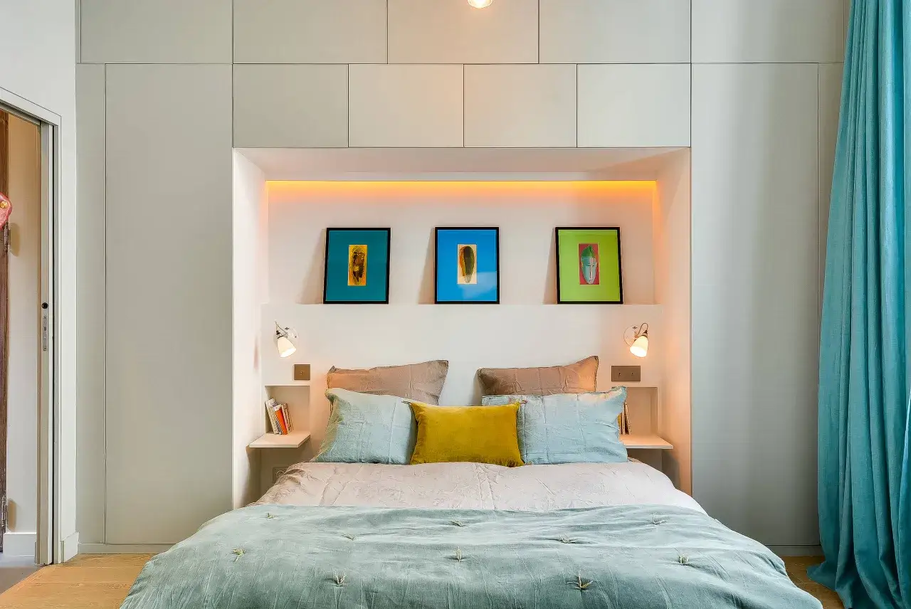 Idee salvaspazio camera da letto piccola: letto incassato con nicchia illuminata, quadri colorati e tende turchesi.
