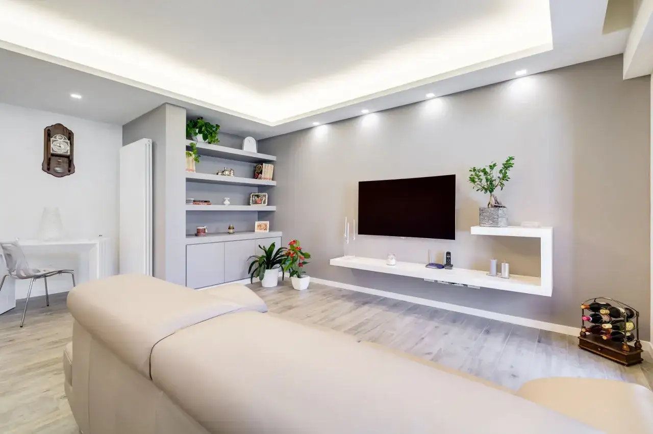 Soggiorno moderno con divano chiaro, TV a schermo piatto su mensola fluttuante e una parete in cartongesso con libreria integrata.