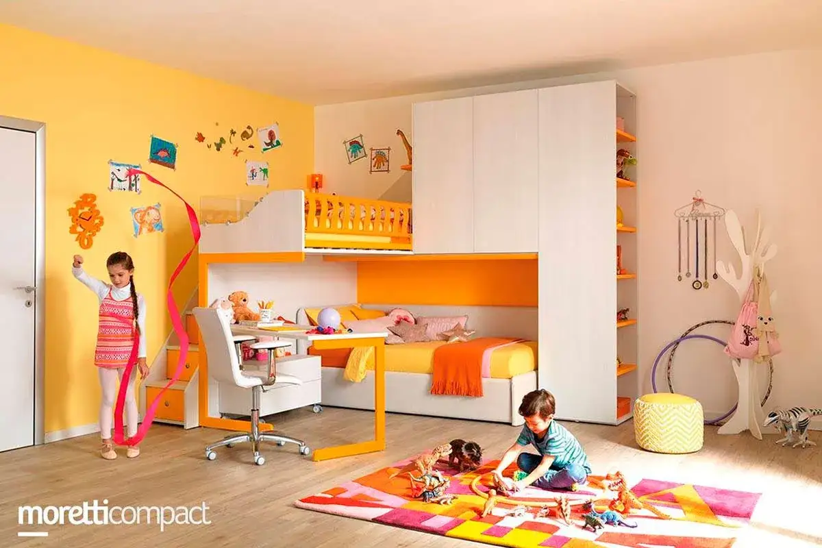 Bambini giocano in una stanza colorata con letti a castello e armadi. Ecco come sistemare i giochi in salotto per un ambiente ordinato e divertente.