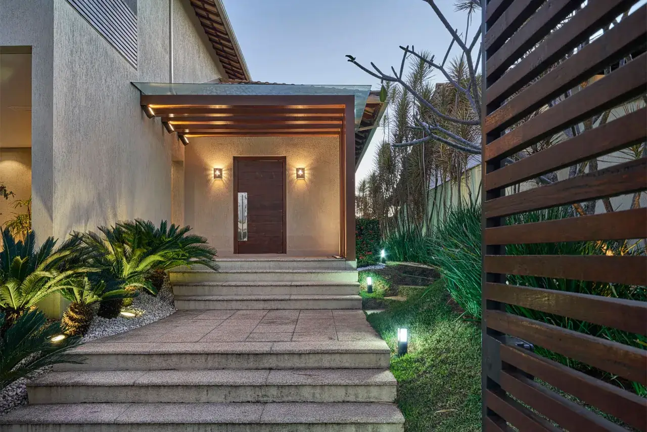 Moderne idee portico entrata casa esterno: gradini in pietra, porta in legno scuro, tettoia con travi a vista e illuminazione soffusa che valorizza le piante.