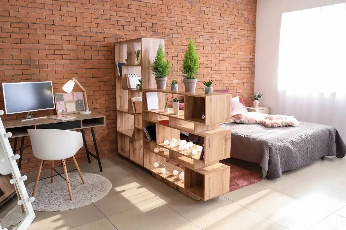 Un ambiente moderno con una cucina e camera da letto insieme, separate da una libreria in legno. Parete in mattoni a vista.