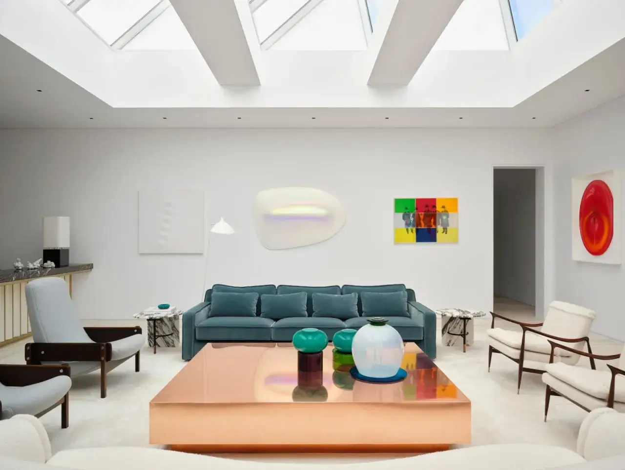 Soggiorno moderno con divano blu petrolio, tavolino in rame, sedie in bouclé e opere d'arte astratte. Ottime idee arredamento soggiorno.