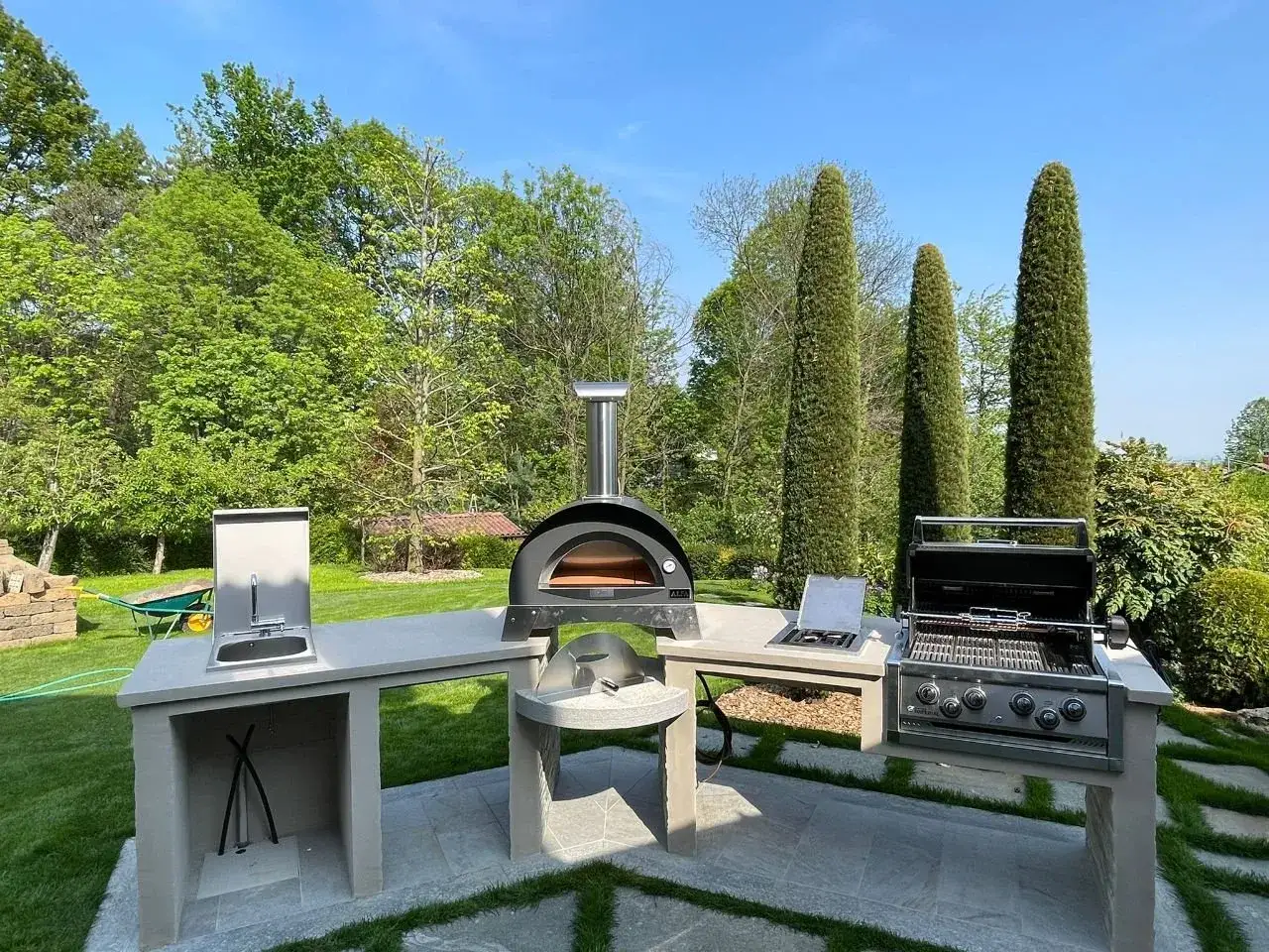 Una splendida zona barbecue esterna con forno per pizza, griglia e lavello, pronta per grigliate estive.