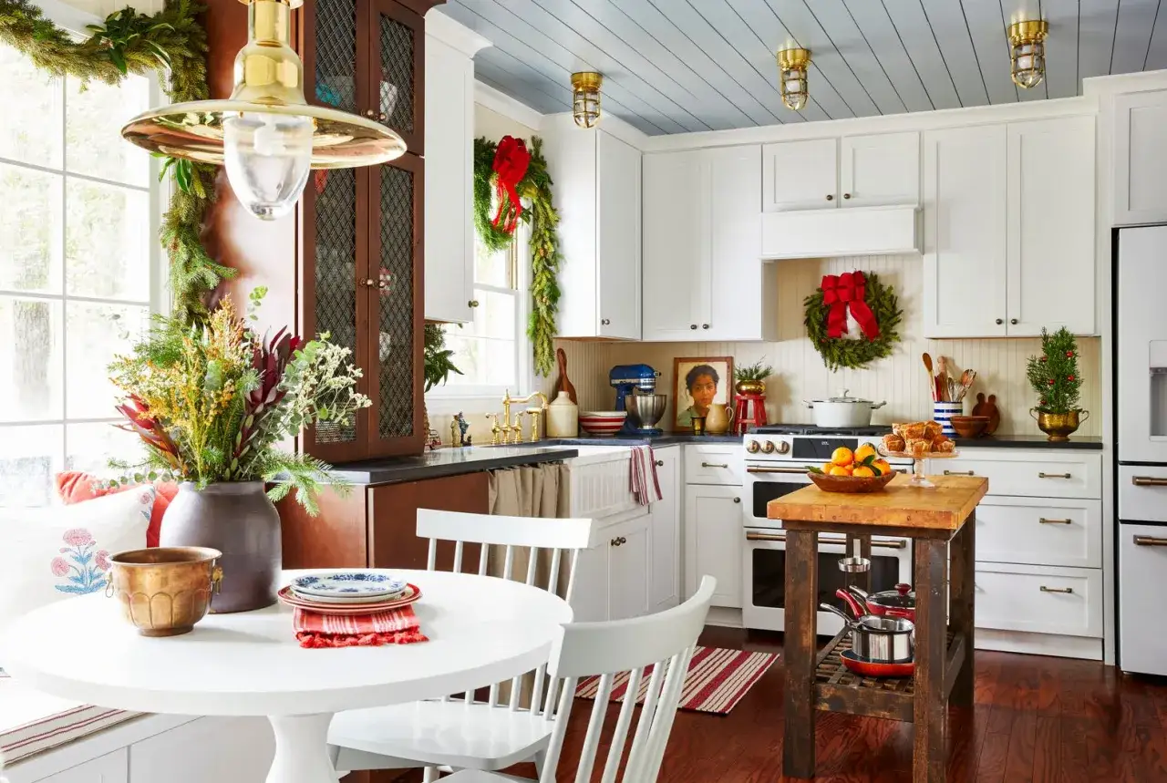 Ecco come addobbare la cucina per Natale: ghirlande verdi, fiocchi rossi e un albero in vaso creano un'atmosfera festosa.