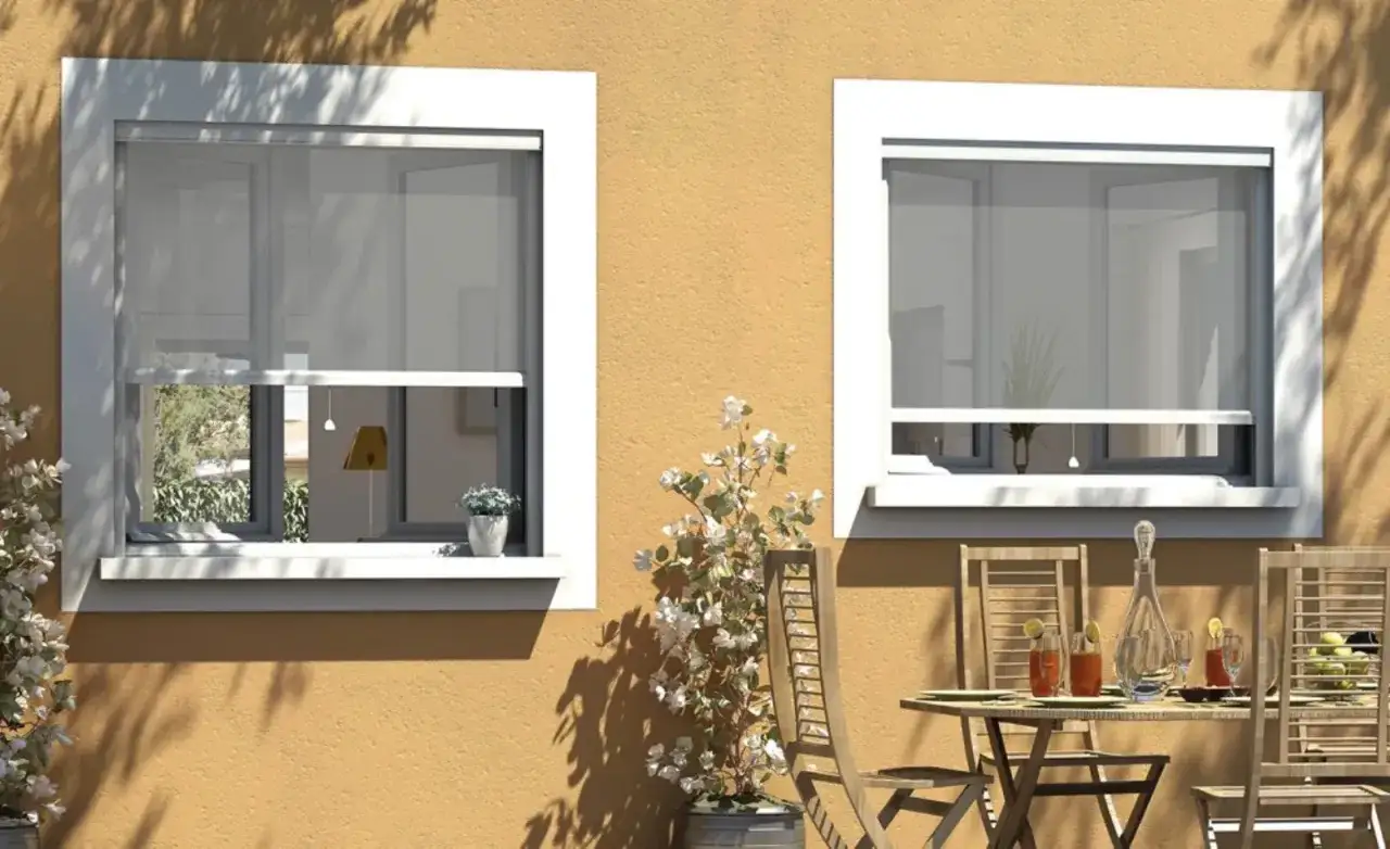 Finestre con zanzariere fai da te, un tavolino apparecchiato all'esterno, fiori bianchi e un muro color ocra.