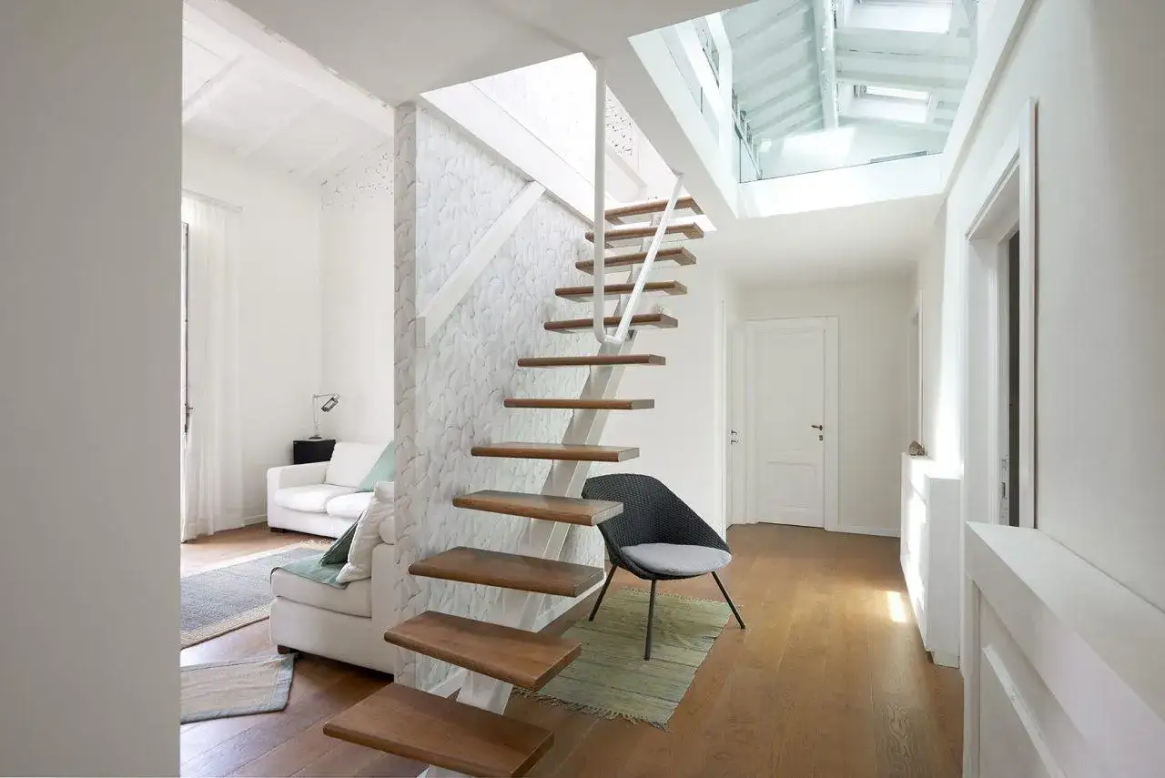 Scala interna moderna in legno e metallo, con design a sbalzo. L'ambiente luminoso, con tetto a vista e lucernari, rispetta la normativa scale interne uso privato.