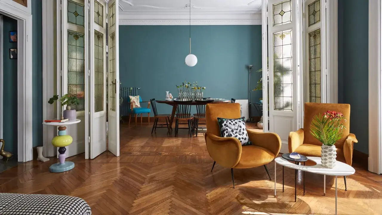 Living room with vintage and modern furniture, featuring velvet armchairs, a dining table, and stained-glass doors.