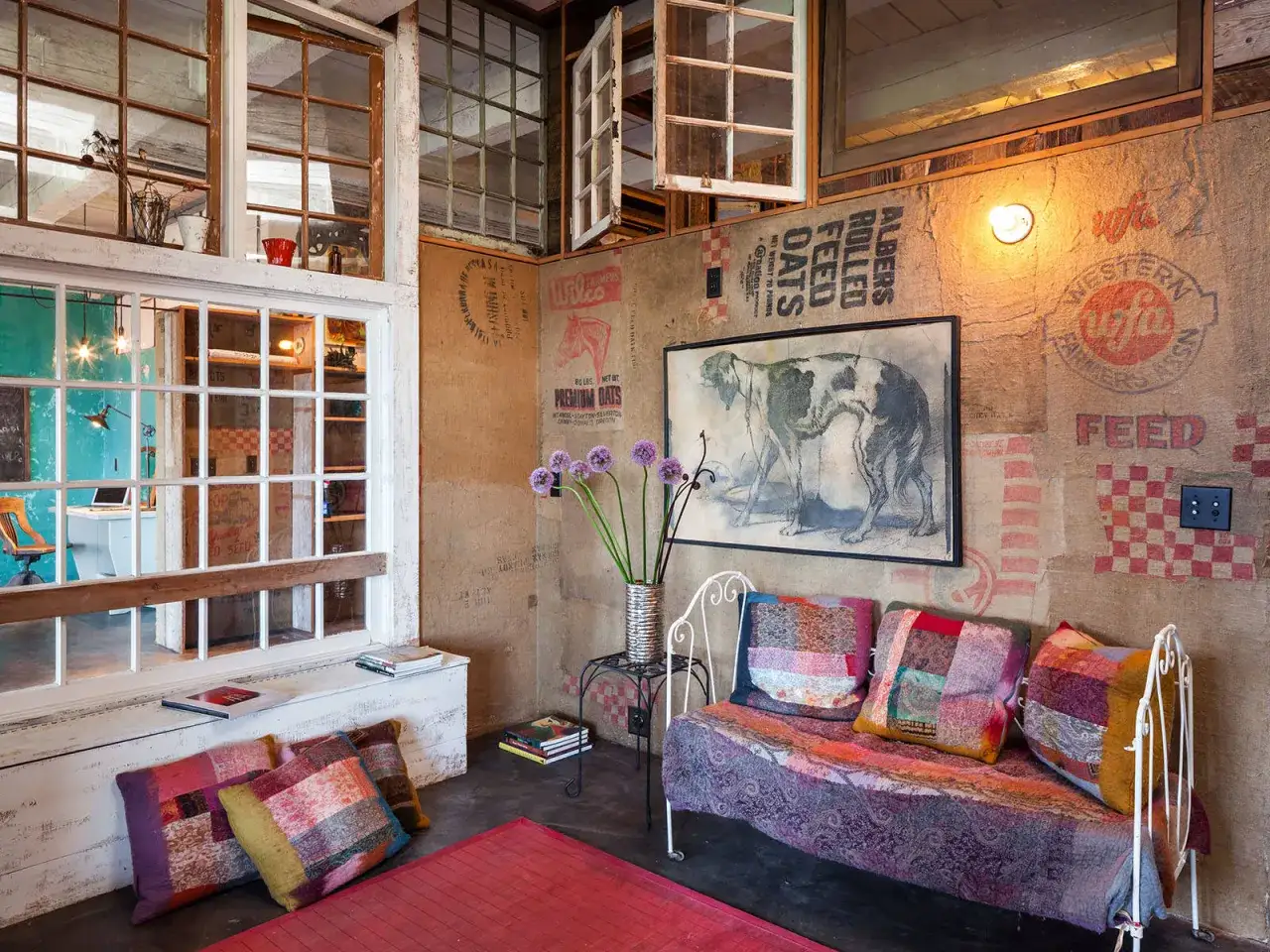 Un divano colorato e cuscini patchwork in una casa stile bohemien con pareti di sacchi di iuta e un quadro di un cane.