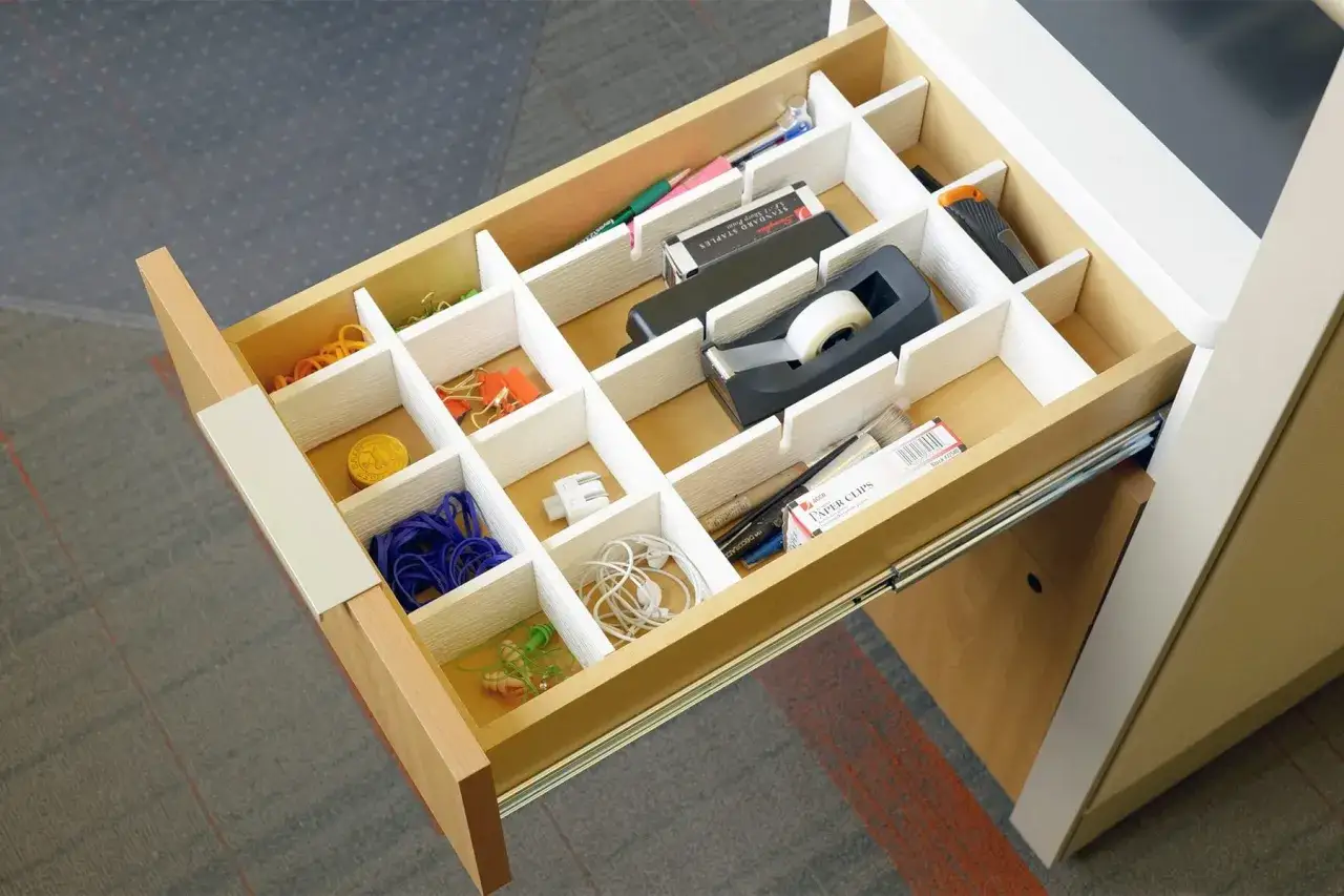 Organizzare la scrivania: come fare divisori per cassetti fai da te. L'immagine mostra un cassetto aperto con divisori bianchi che separano elastici, graffette, nastro adesivo e altri piccoli oggetti.