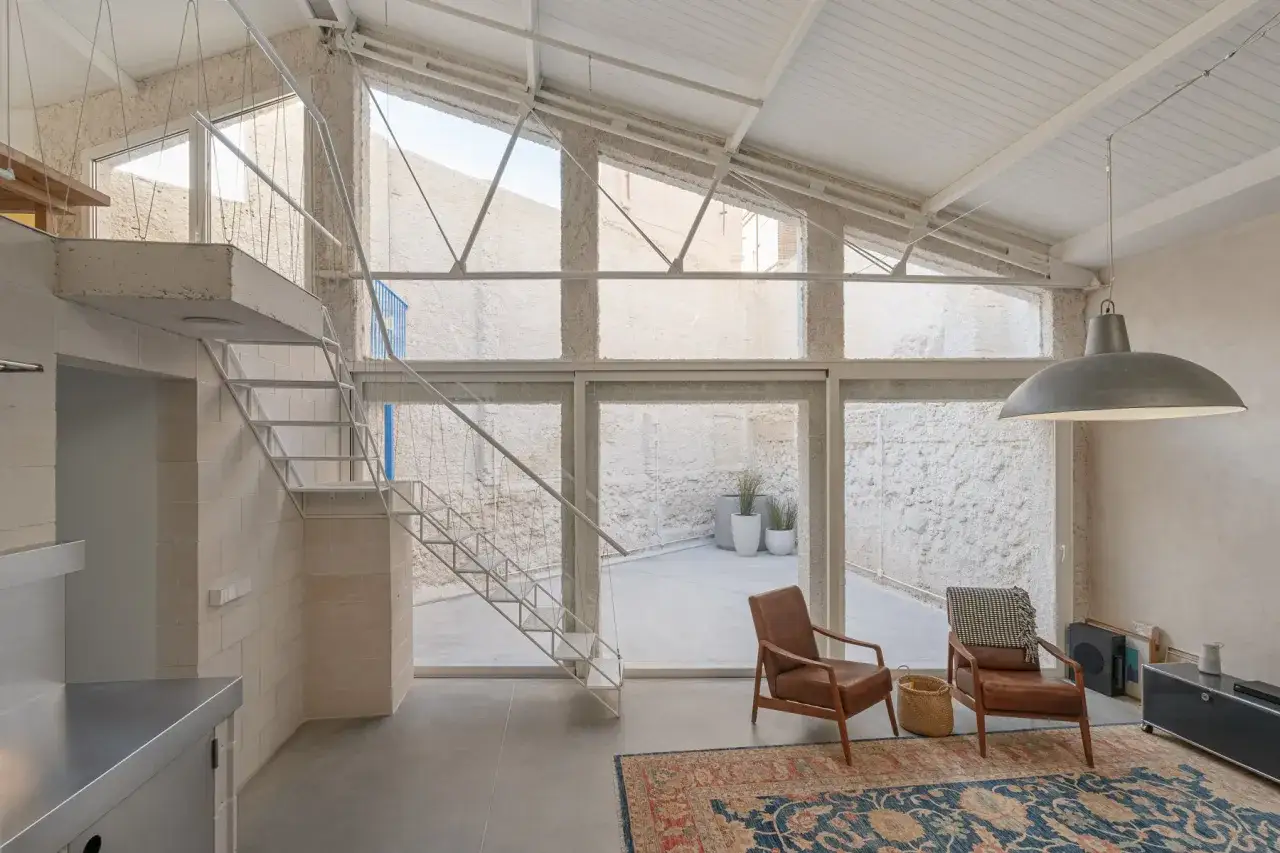 Interno moderno con scala a vista, due poltrone in pelle e un grande lampadario. Perfetto esempio di cambio destinazione d'uso da magazzino ad abitazione.