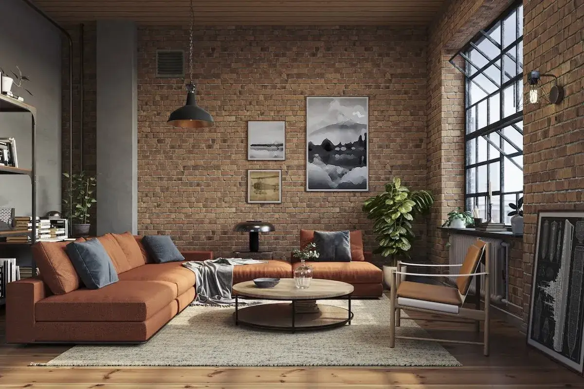 Soggiorno con divano arancione, tavolino rotondo e poltrona in legno. Pareti in mattoni a vista e grande finestra, tipico arredamento industrial.