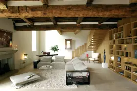 Soggiorno con soffitto con travi in legno a vista, camino in pietra, divano, libreria e scala in legno.