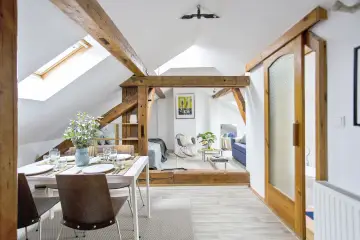 Soggiorno mansardato con **cartongesso soffitto travi a vista**, zona pranzo e salotto con divano blu.
