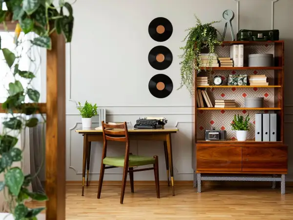 Scrivania con macchina da scrivere e sedia verde, libreria con dischi in vinile e piante. Perfette idee arredamento vintage per un angolo studio.