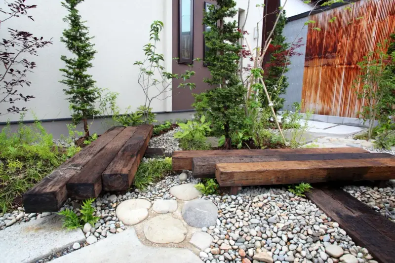 Un piccolo giardino zen con panchine in legno riciclato, ghiaia e piante verdi. Perfetto per idee giardino piccolo fai da te.